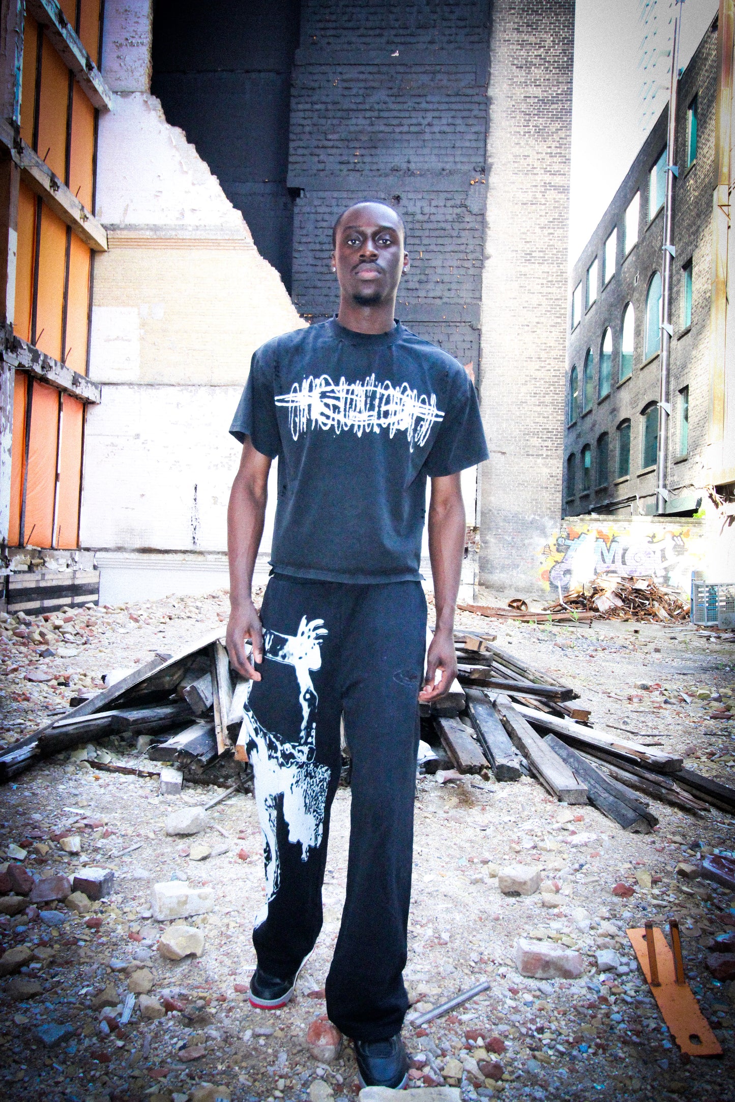 Man wearing a dark t-shirt and pants with graphic designs in an urban setting